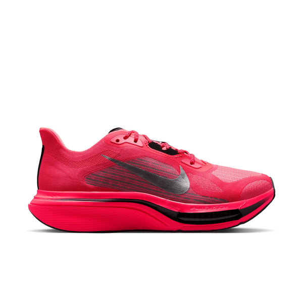 En livlig Nike Pegasus Plus 2-løbesko til kvinder i farven Flash Crimson med et Nike Swoosh-logo i metallisk sølv og sort, snørelukning, en åndbar overdel i mesh og en tyk lyserød sål med responsiv ZoomX-skumstøddæmpning. Skoen er afbildet i sideprofil på en hvid baggrund.