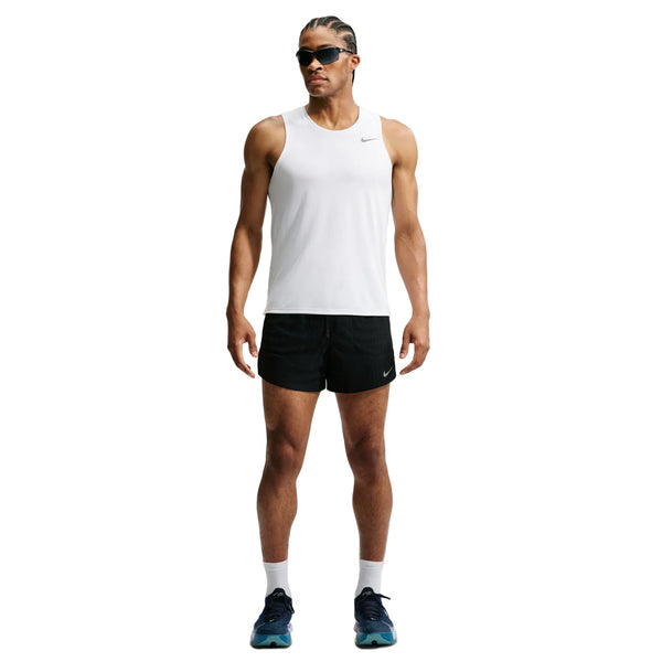 En person står med ansigtet vendt fremad og er iført en hvid, ærmeløs sportstrøje, Nike Aero-FIT 5" løbeshorts med indvendig linning til mænd i farverne sort/reflekterende sølv, hvide sokker, sorte løbesko med ventilationsteknologi samt solbriller. Baggrunden er ensfarvet hvid.