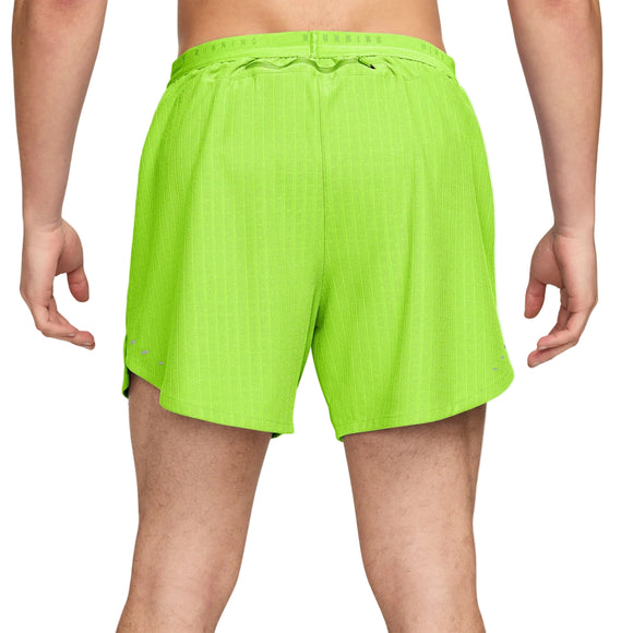 Der ses en person fra livet og ned, iført lysegrønne Nike Aero-FIT 5" løbeshorts med indvendig underbuks, Herre, i farven Volt/Reflective Silver – et stilfuldt par løbeshorts til mænd med snøre – stående med armene afslappet ned langs siden.