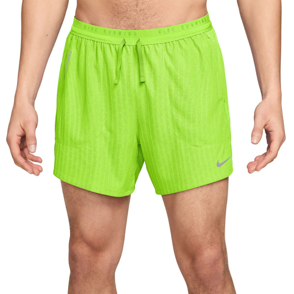 En person iført Nike Aero-FIT 5" løbeshorts til mænd i farven »Bright Volt« med en reflekterende sølvfarvet Nike-logo på venstre ben. Disse herre-løbeshorts byder på komfort og stil med deres klassiske 5" design og praktiske underbuksforing.