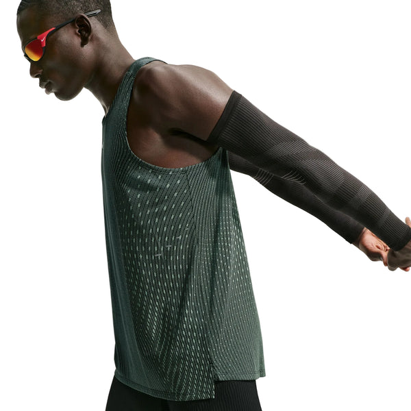 En person iført en Nike Aero-FIT løbetop til mænd i farvekombinationen sort/lysegrøn Spark/reflekterende sølv samt sorte armvarmere og røde sportsolbriller strækker armene bag ryggen foran en ensfarvet hvid baggrund og viser dermed en letvægts-løbetop fra Nike, der er designet til maksimal ventilation.