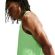 En mand med mellemlange dreadlocks har en Nike Aero-FIT løbetanktop til mænd i farverne Volt/Light Silver/Reflective Silver på. Han står vendt mod venstre og kigger nedad foran en hvid baggrund.