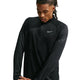 En person med langt, flettet hår har en sort Nike Aero-FIT 1/2-Zip løbetrøje på, Herre, Sort/Reflekterende Sølv – en åndbar løbetrøje med en kvart lynlås. Det reflekterende sølvfarvede Nike-swoosh-logo ses på venstre bryst. Personen kigger ned med armene over kors.