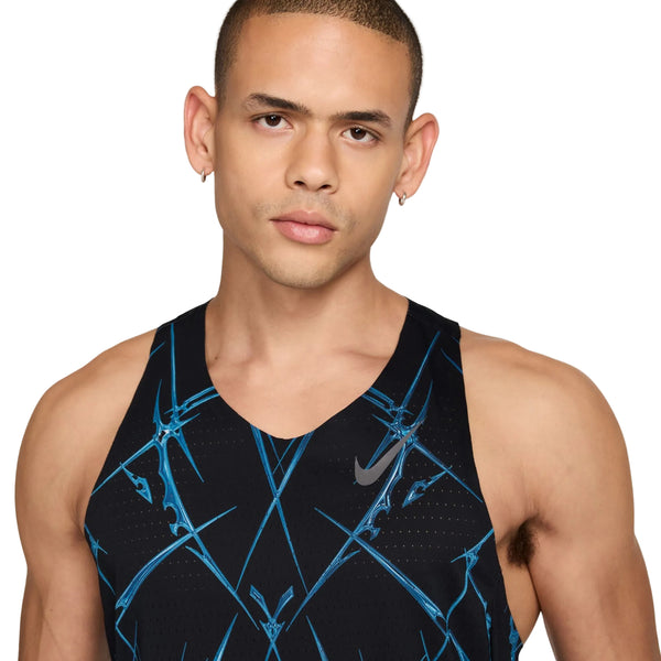 En person med kort hår og øreringe har en Nike AeroSwift Printed Running Singlet, Herre, i sort/hvid på, med et geometrisk mønster og logo, mens vedkommende står foran en hvid baggrund.