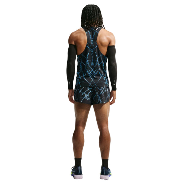 En person med langt hår står med ryggen til kameraet og er iført en ærmeløs sort og blå sportstrøje, Nike AeroSwift Printed 2" løbeshorts med indvendig underbuks til mænd i sort/hvid, sorte armvarmere, strømper og sportssko på en hvid baggrund.