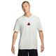 En person med kort hår har en ensfarvet Summit White Nike ACG Dri-FIT T-shirt på, hvor der er et lille rødt trekantlogo placeret midt på brystet. Personen står foran en hvid baggrund med et neutralt udtryk i ansigtet.