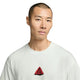 En person med kort hår har en Nike ACG Dri-FIT T-shirt, Herre, i farven Summit White på, med et rødt, trekantet ACG-motiv. Baggrunden er ensfarvet hvid.