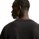 Der ses en person set bagfra og lidt fra siden, iført en sort Nike ACG Dri-FIT T-shirt til mænd. Baggrunden er hvid, og personens ansigt er delvist synligt i profil, mens vedkommende kigger ud mod venstre.