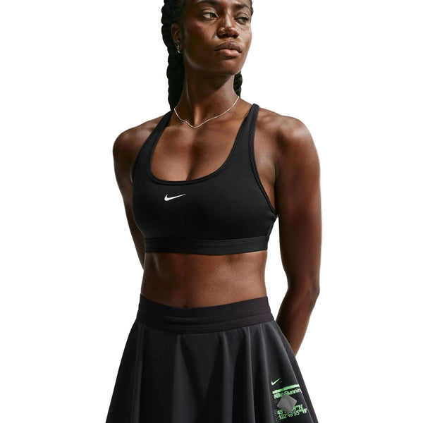 En kvinde iført en sort Nike-sport-bh og Nike Swift Dri-FIT løbeskort, Dame, sort/sort/reflekterende sølv, står med armene bag ryggen og kigger til siden.