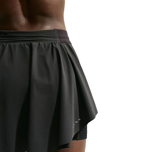 Et nærbillede af en person, der bærer Nike Swift Dri-FIT løbeskirt til kvinder, sort/sort/reflekterende sølv, fotograferet foran en ensfarvet hvid baggrund.