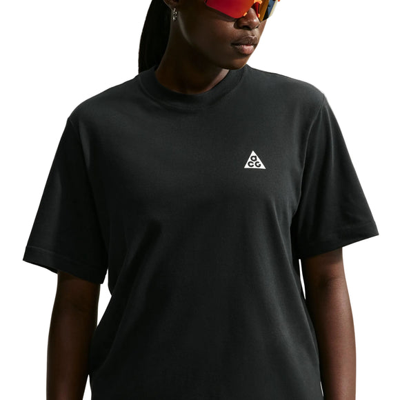 En person iført en sort Nike ACG Dri-FIT T-shirt til kvinder med et lille hvidt trekantet logo på brystet og røde solbriller står foran en hvid baggrund.