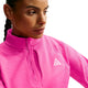 En person iført Nike Therma-FIT 1/2-Zip Top til kvinder i farverne Desert Pink, Light Orewood Brown og Summit White. Den langærmede top har et design i gitterfleece, en halv lynlås foran og er prydet med Nike ACG-logoet. Personen har håret sat i en fletning og kigger let til siden foran en ensfarvet hvid baggrund.