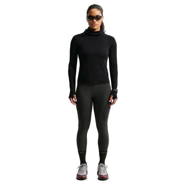 En person iført en sort Nike Wool Running Mid-Layer Top, Dame-model med manchetter med tommelfingerhuller, sorte leggings og grå løbesko.