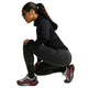 En person iført en sort Nike Wool Running Mid-Layer Top og leggings sidder på hug med løbesko på.