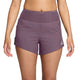 En kvinde har Nike ACG Dri-FIT Trail-løbeshorts med mellemhøj talje og indvendig underbuks i farvekombinationen Violet Dust/Mineral Slate/Summit White på. Shortsene har en mellemhøj talje og et lille hvidt Nike-logo på venstre ben. Billedet set forfra viser hende fra taljen til midt på låret, med hænderne afslappet ned langs siden, hvilket fremhæver disse stilfulde løbeshorts til kvinder.