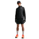 En person iført sort jakke, Nike ACG "Second Sunrise" 5" Brief-Lined Shorts i Black/Anthracite/Summit White, sorte handsker, sort kasket, orange solbriller, hvide sokker og knaldorange løbesko står på en almindelig hvid baggrund.