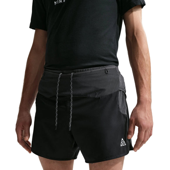 En person er iført sorte Nike ACG "Second Sunrise" 5" Brief-Lined Shorts i Black/Anthracite/Summit White med et lille trekantlogo og zigzag-snøre, sammen med en sort T-shirt. Hovedet er ikke synligt på billedet.