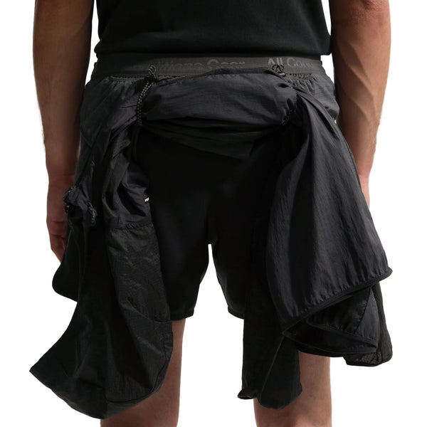 En person i Nike ACG "Second Sunrise" 5" Brief-Lined Shorts (Black/Anthracite/Summit White) med en sort jakke bundet i taljen, vist bagfra med kun underkroppen og overbenene synlige.