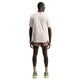 En person står med ryggen til kameraet iført en lyserød Nike ACG Dri-FIT ADV Trail Running Top til mænd i farven Lt Orewood Brn/Summit White, brune sportsshorts, lysebrune sokker, grønne sneakers, et smartwatch og solbriller. Baggrunden er helt hvid.