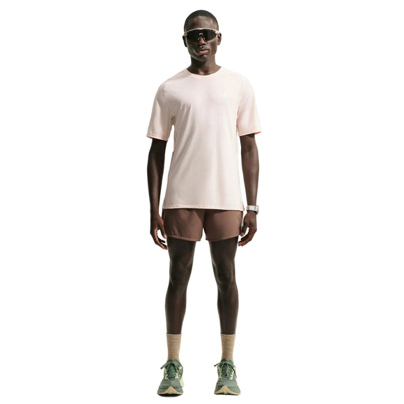 En mand står med ansigtet vendt fremad iført en lysbeige Nike ACG Dri-FIT ADV Trail Running Top, Herre, Lt Orewood Brn/Summit White – ofte kaldet en trailløb-T-shirt til mænd – kombineret med brune shorts, beige sokker, grønne sneakers, sorte solbriller og et armbåndsur, foran en hvid baggrund.