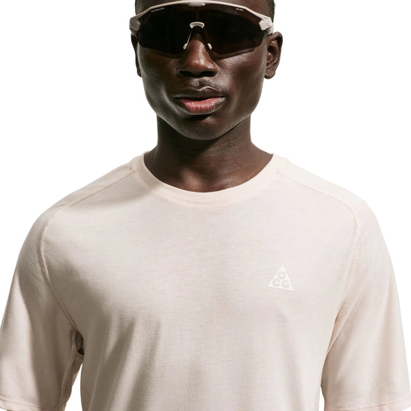 Der ses et billede af en person fra skuldrene og opefter på en hvid baggrund. Personen bærer store sorte solbriller og en lys Nike ACG Dri-FIT ADV Trail Running Top, Herre, i farven Lt Orewood Brn/Summit White, som har et lille ACG-logo på brystet.