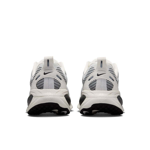 Et par Nike Vomero 18-damesko i farvekombinationen Summit White/Metallic Silver-Sail vises set bagfra, hvor det ikoniske Nike-logo, de åndbare mesh-paneler og de strukturerede såler, der er udviklet til maksimal dæmpning, fremhæves. Skoene er placeret side om side på en ensfarvet hvid baggrund.