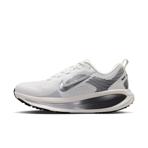 Et sidebillede af Nike Vomero 18 Dame i farvekombinationen Summit White/Metallic Silver-Sail, med en hvid overdel med et metallisk sølvfarvet Swoosh-logo, sorte og grå detaljer, hvide snørebånd og en sort-hvid ydersål, vist på en ensfarvet hvid baggrund. Denne Nike-model er kendt for at være blandt de mest komfortable løbesko til både mænd og kvinder.