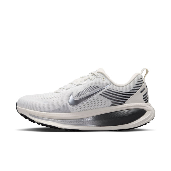 Et sidebillede af Nike Vomero 18 Dame i farvekombinationen Summit White/Metallic Silver-Sail, med en hvid overdel med et metallisk sølvfarvet Swoosh-logo, sorte og grå detaljer, hvide snørebånd og en sort-hvid ydersål, vist på en ensfarvet hvid baggrund. Denne Nike-model er kendt for at være blandt de mest komfortable løbesko til både mænd og kvinder.
