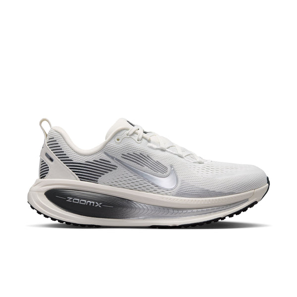 En Nike Vomero 18-løbesko til kvinder i farvekombinationen Summit White/Metallic Silver-Sail, med et metallisk sølvfarvet Nike-swoosh, sorte og grå detaljer på hælen samt »ZoomX«-logoet på den sorte mellemsål. Skoen giver maksimal dæmpning takket være den polstrede overdel i mesh og den slidstærke ydersål i gummi.