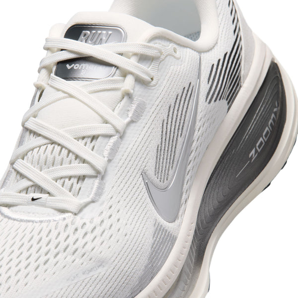 Nærbillede af en Nike Vomero 18-løbesko til kvinder i farvekombinationen Summit White/Metallic Silver-Sail med grå og sølvfarvede detaljer, overdel i mesh, synlige snørebånd, Zoom Air-sål for maksimal dæmpning samt det karakteristiske Nike Swoosh-logo på siden. På tungen står der »RUN« og »VOMERO«.