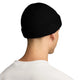 Der ses en person set bagfra, der bærer en sort Nike ACG Terra Beanie – et unisex-tilbehør, der nemt kan kombineres med en frisk, hvid skjorte. Personens korte hår og den lille ringørering i venstre øre tilføjer et diskret stilfuldt touch, mens den ensfarvede hvide baggrund holder fokus på dette ubesværet cool look.