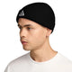 En person, der bærer en sort Nike ACG Terra Beanie – en unisex-hue med et hvidt, trekantet logo – kombineret med en ensfarvet hvid skjorte og vendt mod venstre. Huen dækker personens ører, og vedkommende har en lille ringørering i venstre øre.