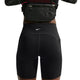 Der ses en person fra taljen til midt på låret iført Nike High-Waisted 7" løbeshorts med lommer i sort/reflekterende sølv og en sort bæltetaske. Personen har armene løftet, hvilket delvist afslører overkroppen.