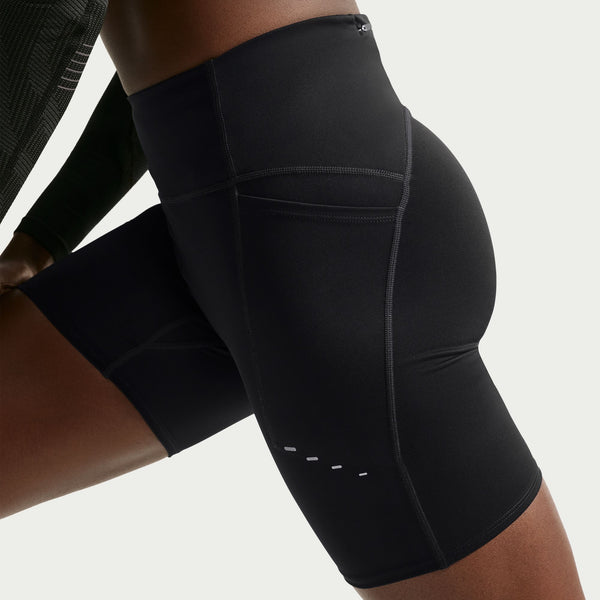 En person har Nike High-Waisted 7" løbeshorts med lommer i sort/reflekterende sølv på, der har en tætsiddende pasform, synlige sømme og en lille reflekterende detalje ved låret; billedet viser shortsene fra taljen til midt på låret på en ensfarvet lys baggrund.