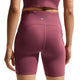 Der ses en person set bagfra iført Nike High-Waisted 7″ løbeshorts med lommer i farven Pink Smoke/Reflective Silver, kombineret med en matchende crop top. Nike-logoet er placeret på shortsenes linning, og personen står med armene afslappet ned langs siden.