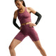 En person står i en atletisk stilling iført Nike Dame High-Waisted 7″ løbeshorts med lommer i farven Pink Smoke/Reflective Silver. Personen har desuden sorte armvarmere på, og baggrunden er ensfarvet hvid.