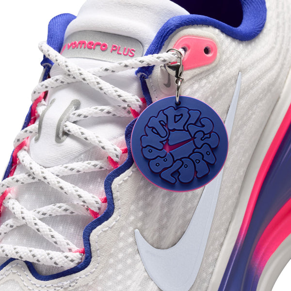Nærbillede af Nike Vomero Plus Dame i White/Metallic Silver-Concord-Hyper Pink med hvide snørebånd, der er trukket gennem lyserøde øjer, og et rundt blåt og lilla mærke med stiliseret tekst for maksimal komfort.