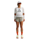 En person står foran en hvid baggrund iført en hvid Dri-FIT ADV-langærmet trøje i mesh med et trekantet logo på brystet, Nike ACG »Trailwind«-shorts i farven Dame Light Army/White, orange sokker, lyse sneakers, en visir og solbriller.