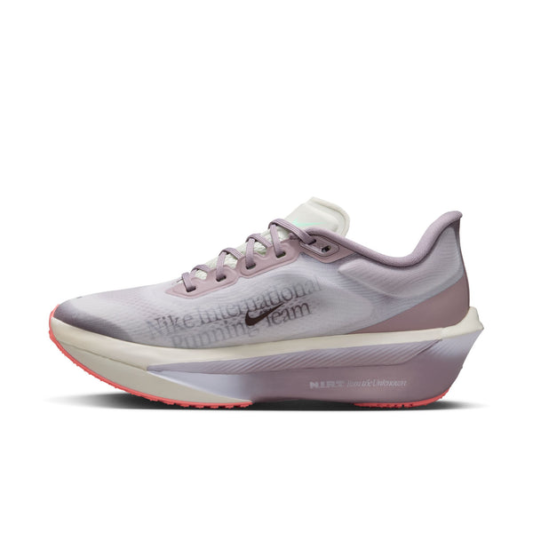Et sidebillede af Nike Zoom Fly 6 Dame-løbeskoen i farvekombinationen Lt Violet Ore/Baroque Brown-Sea Glass, der har en tyk sål, synlige snørebånd og teksten »Nike International Running Team« på overdelen. Denne løbesko fra Nike, der her vises på en ensfarvet hvid baggrund, er designet med fokus på både ydeevne og stil.