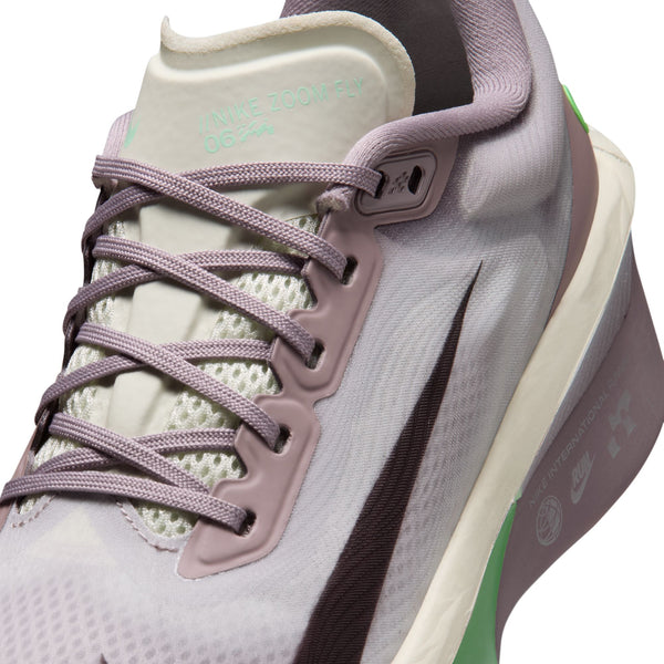 Nærbillede af Nike Zoom Fly 6 Dame-løbeskoen i farvekombinationen Light Violet Ore/Baroque Brown–Sea Glass, med et stort sort Swoosh-logo, lavendelblå snørebånd, overdel i mesh og en grøn detalje på hælen. Denne carbon-sko har tydelige Nike-mærker og -logoer på både tungen og siden.