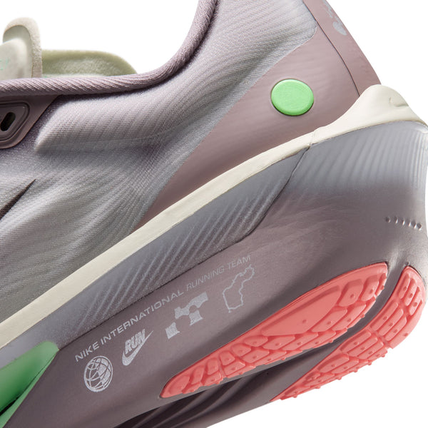 Nærbillede af hælen og siden på den lysviolette Nike Zoom Fly 6 Dame-løbesko i farvekombinationen Lt Violet Ore/Baroque Brown-Sea Glass med grønne og koralfarvede detaljer. Tekst og logoer, herunder »NIKE INTERNATIONAL RUNNING TEAM«, er trykt på sålen.