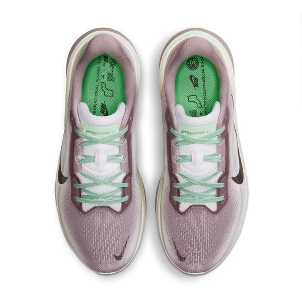 Et par Nike Pegasus 42-løbesko til kvinder i farvekombinationen Light Violet Ore/Baroque Brown-Sea Glass, med grønne indlægssåler, hvide snørebånd og sorte Nike Swoosh-logoer samt en responsiv mellemsål af ReactX-skum, set ovenfra på en hvid baggrund.