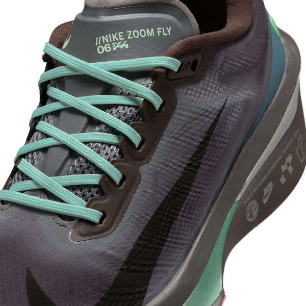 Nærbillede af Nike Zoom Fly 6 herresko i farvekombinationen Baroque Brown/Black-Smoke Grey-Ironstone med det karakteristiske logo på siden. Overdelen fremstår i et sofistikeret gråt og sort farveskema med et struktureret design, der fremhæver Nikes innovative carbonsko-teknologi, der sikrer forbedret ydeevne.