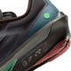 Nærbillede af hælen på Nike Zoom Fly 6 Herre i farvekombinationen Baroque Brown/Black-Smoke Grey-Ironstone, der fremhæver den strukturerede ydersål, teksten »Nike International Running Team« og forskellige logoer. Skoen har et elegant design i kulfiber med mørke og blågrønne nuancer, en grøn prikdetalje og synlige brune snørebånd.