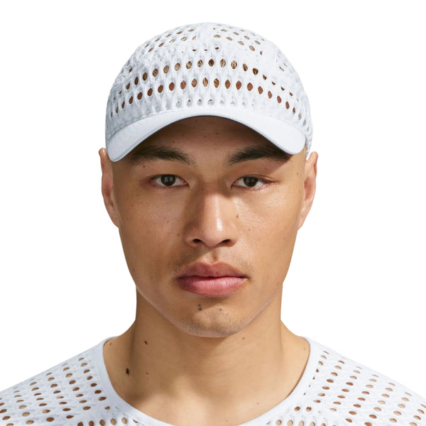 En person, der bærer en hvid Nike ACG Radical AirFlow Fly-kasket med et perforeret, gitterlignende mønster.