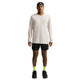 En mand står med ansigtet vendt fremad iført en Nike Dri-FIT langærmet løbetrøje, Herre, i farven Light Bone, samt sorte shorts, neongule sokker, sorte sneakers og en sort kasket, der er vendt bagud. Baggrunden er ensfarvet hvid.