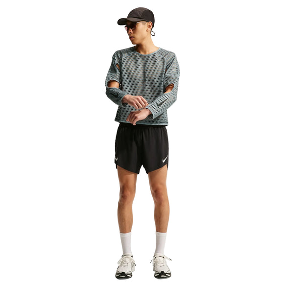 En person iført en grå Nike Stride Aero-FIT langærmet løbetrøje, Herre, Cool Grey/Black med udskæringer ved albuerne, sorte sportsshorts, en kasket og løbesko.