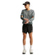 En person iført en grå Nike Stride Aero-FIT langærmet løbetrøje, Herre, Cool Grey/Black med udskæringer ved albuerne, sorte sportsshorts, en kasket og løbesko.