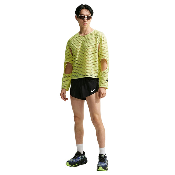 En mand har en limegrøn, langærmet Nike Stride Aero-FIT langærmet løbetrøje, Herre, Lt Lemon Twist/Black med udskæringer ved skuldrene på, sammen med sorte løbeshorts og sportssko.