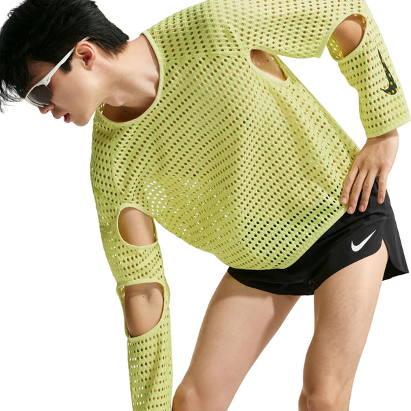 En person iført en limegrøn Stride Aero-FIT langærmet løbetrøje, Herre, Lt Lemon Twist/Black med udskæringer ved albuerne og sorte sportsshorts.
